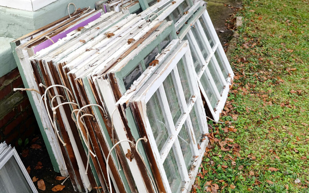 Stack of old weathered window leaning against house